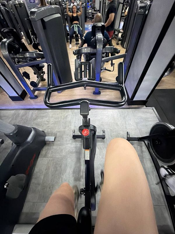 A gym interior featuring varied exercise machines and equipment arranged against windows.