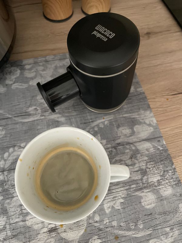 A coffee cup sits on a textured surface next to a coffee maker.