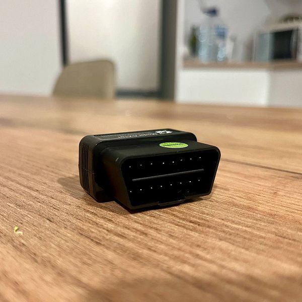 Image of an OBDLINK CX OBD2 Adapter box on a wooden surface with a backdrop of a yellow, black, and white abstract petal-like decoration.