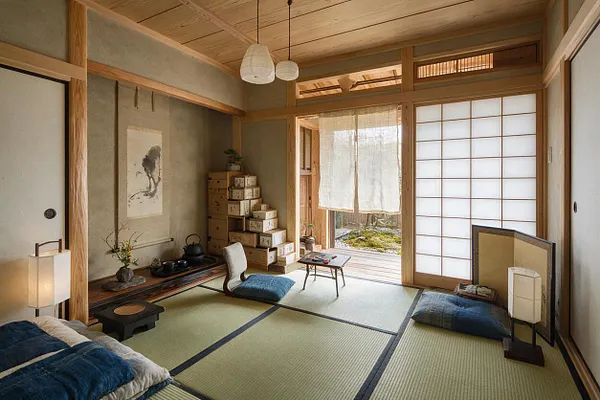 A tranquil Japanese Zen game room with tatami mats, low floor seating cushions, and a small low table at the center. Shoji screens, warm wood framing, paper lantern lights, and a calligraphy artwork create a calm, minimalist atmosphere.