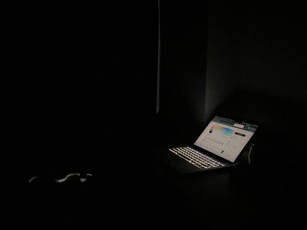 A dimly lit hotel room features a glowing laptop on a desk, highlighting the struggle to navigate in the dark.