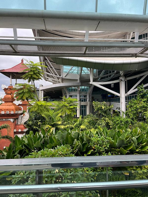 A view of a modern airport structure surrounded by lush greenery and traditional Balinese architecture.
