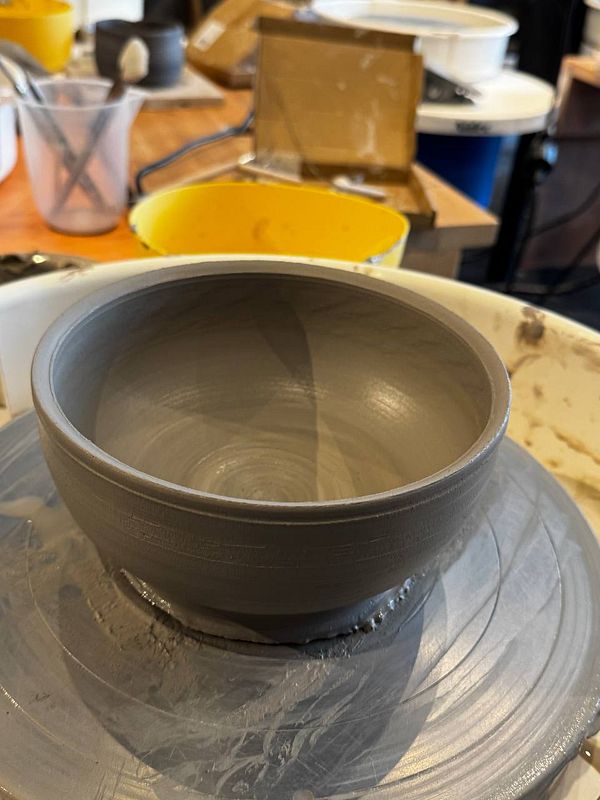 A handmade brown pottery mug with a handle, garnished with a white flower and green leaves, placed on a white surface.