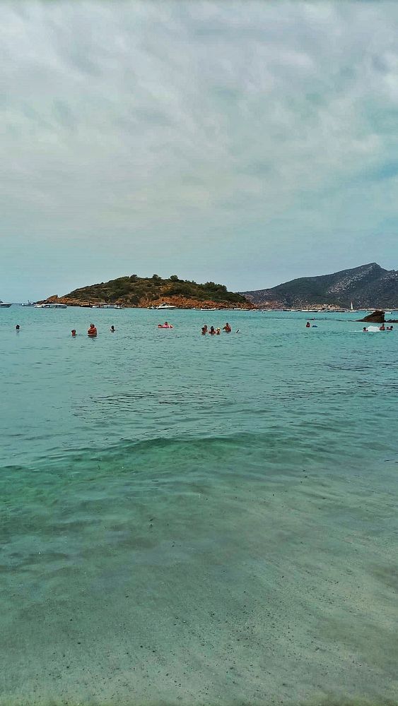 A serene beach scene on a cloudy Sunday with people enjoying the water.