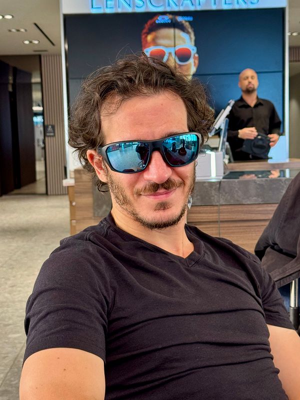 A man wearing new sports sunglasses is seated in a store.