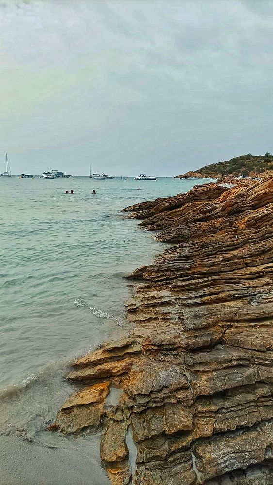 A rocky shoreline meets a calm sea under a cloudy sky.