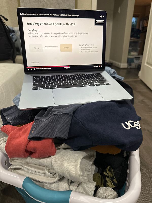 A laundry basket filled with folded clothes sits next to a laptop displaying a workshop presentation.
