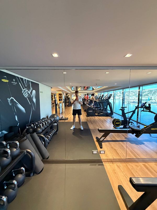 A muscular man lifting a heavy dumbbell in a gym environment, wearing a sleeveless athletic shirt and a watch.