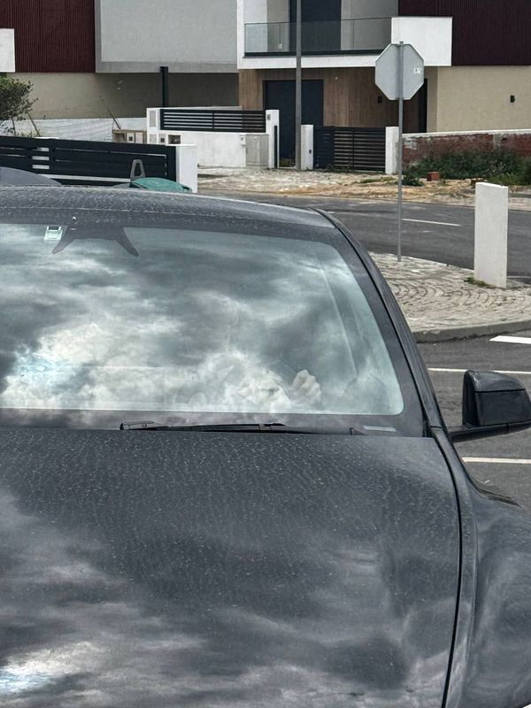 A close-up view of a parked car with a cloudy sky reflected on its windshield.