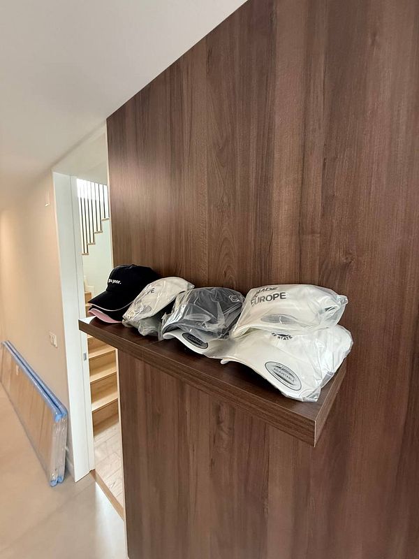 A display of various caps on a wooden shelf in a modern interior space.