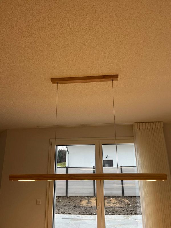 A modern pendant light fixture is being installed in a home setting.