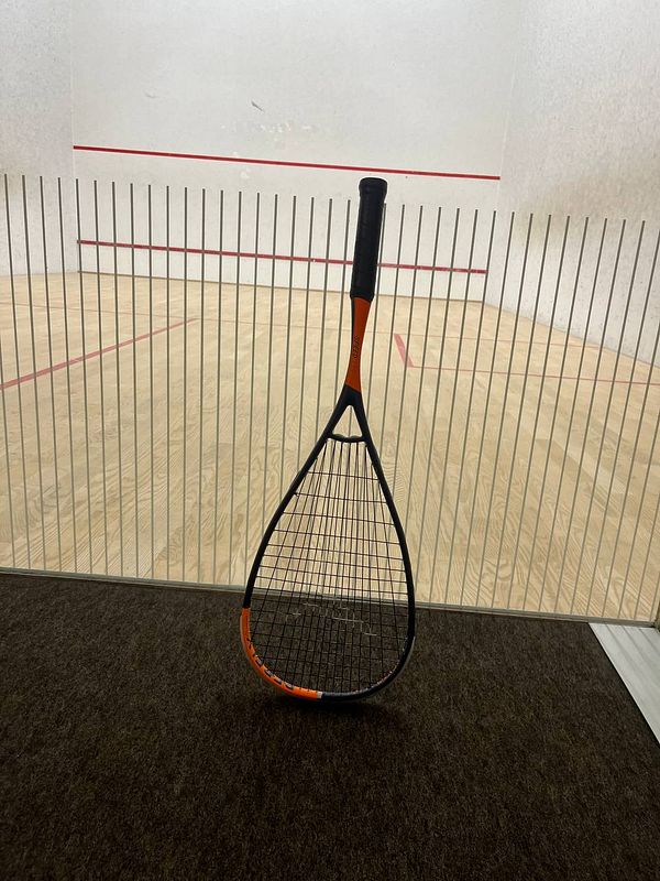 A squash racket is positioned in front of a squash court.