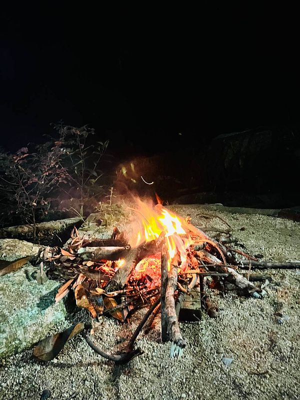 A vibrant campfire is burning brightly in a dark outdoor setting.