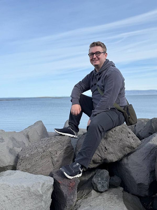 A person is sitting on large rocks by the water in Reykjavik, enjoying the scenic view.