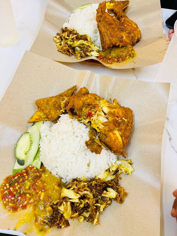 A plate of nasi ayam gepuk featuring fried chicken, rice, and various side dishes.