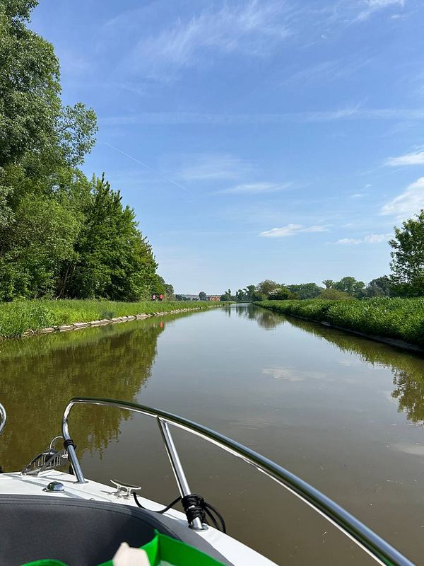 A serene canal scene viewed from a boat, surrounded by lush greenery under a clear blue sky.