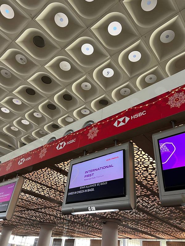 The image captures the interior of an airport check-in area, featuring signage for Air India's first-class services.