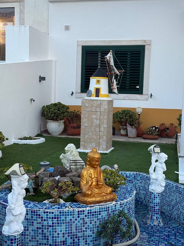 A serene garden scene featuring a golden Buddha statue surrounded by decorative elements.