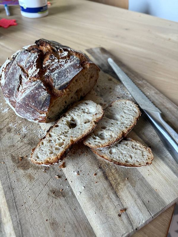 A freshly baked sourdough bread loaf with slices cut and displayed on a wooden cutting board.