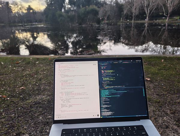 A laptop displaying code is set against a serene lakeside backdrop.