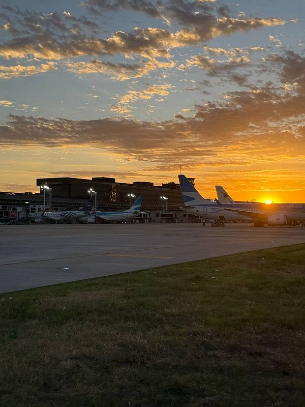 A sunset view at an airport with several airplanes parked on the tarmac.