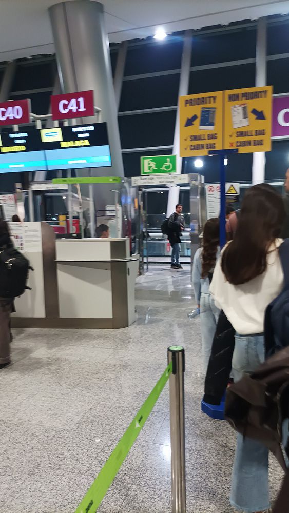 The image captures a busy airport check-in area with passengers waiting in line for a flight to Málaga.
