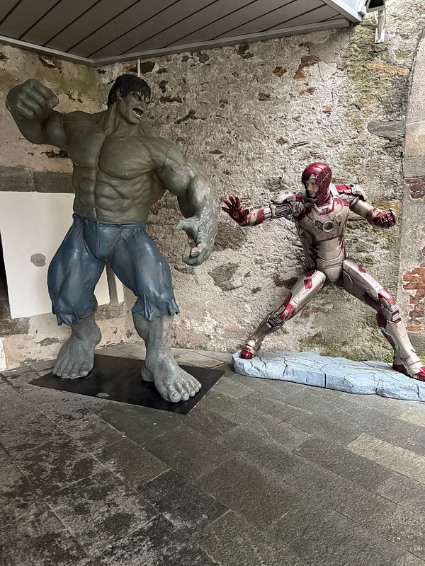 A scene featuring life-sized statues of the Hulk and Iron Man in a stone-walled setting.