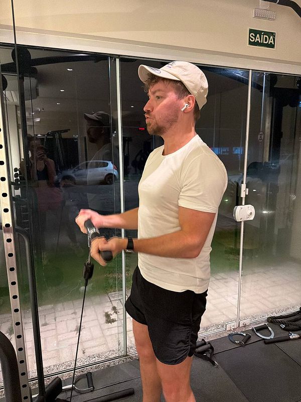 A fluffy white dog is sitting on the floor indoors, wearing a silver glittery collar with a tag.