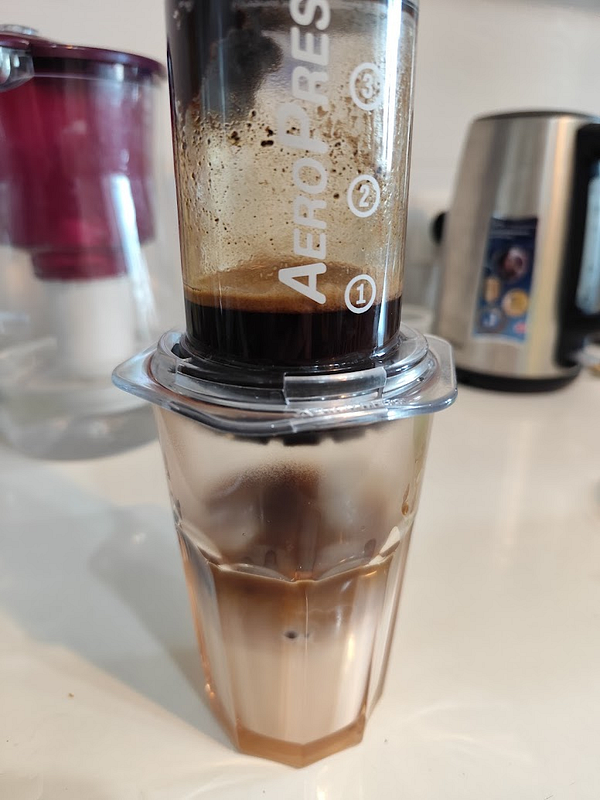 An Aeropress coffee maker is being used to brew coffee into a glass.