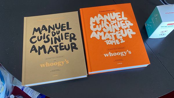 Two cooking books are displayed on a table alongside a small kitchen gadget.