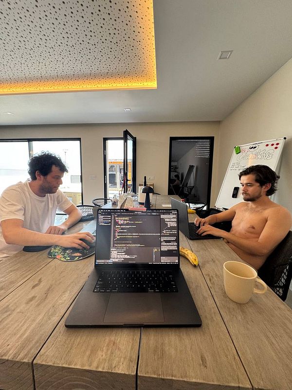 Two individuals are working at a modern coworking space with laptops and a casual atmosphere.