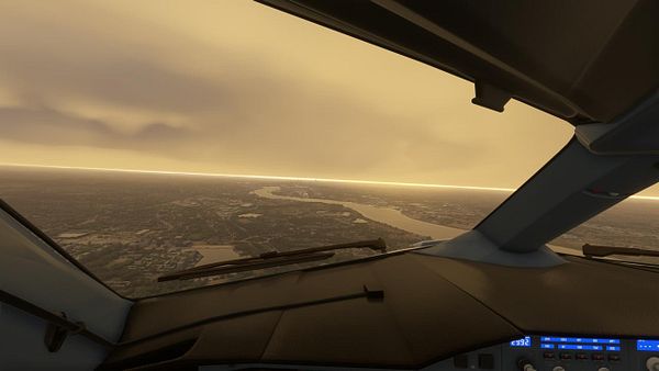 A cockpit view of an aircraft flying over a landscape with a hazy, golden atmosphere.