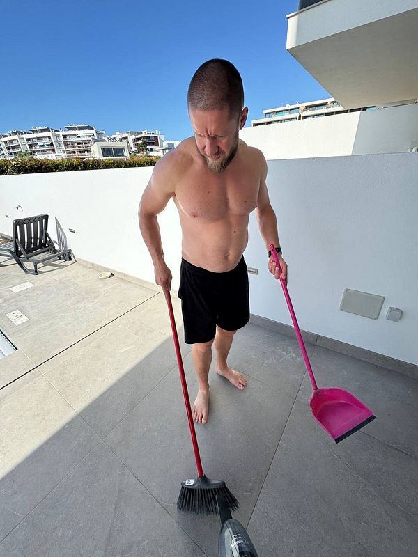 A man is cleaning a patio area while wearing shorts and no shirt.