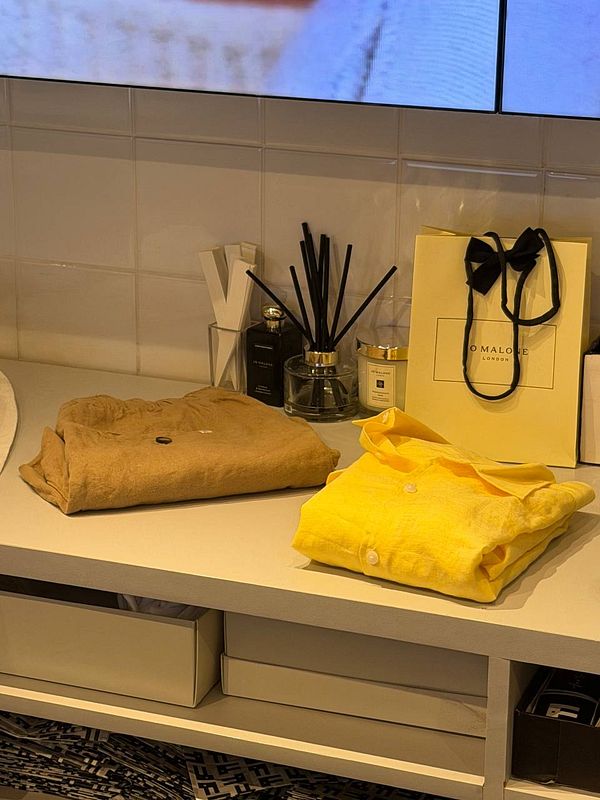 A young woman wearing a white linen shirt and beige linen shorts poses confidently outdoors beside a horse.