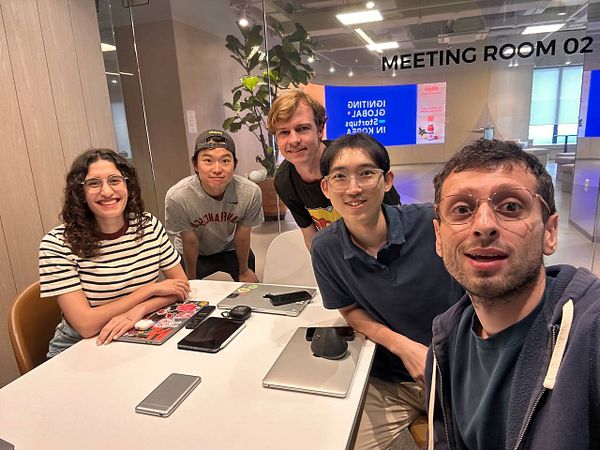 A group of five people poses together in a meeting room.