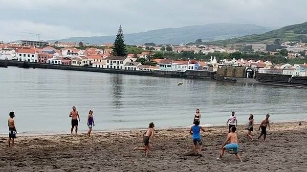 A group of people playing ultimate frisbee on a beach with a scenic backdrop.