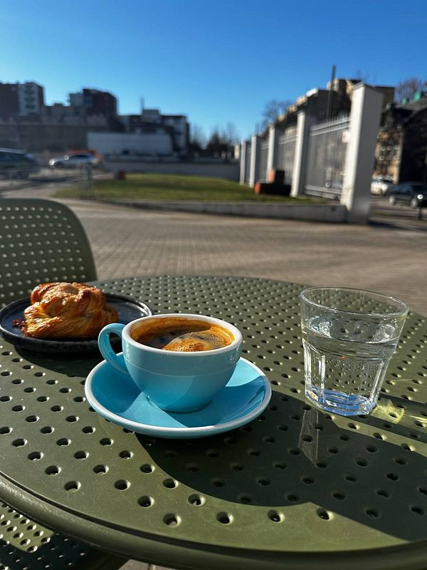 A vibrant outdoor coffee setup featuring a cup of espresso, a pastry, and a glass of water.