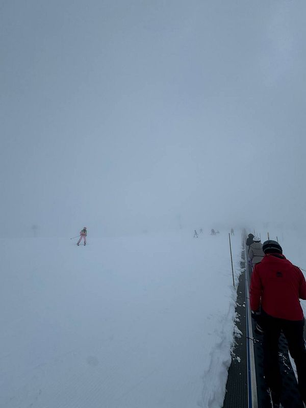 A snowy ski slope shrouded in fog with skiers in the distance.