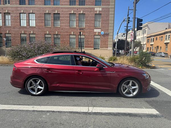 A red sedan is parked at an intersection with a historic building in the background.