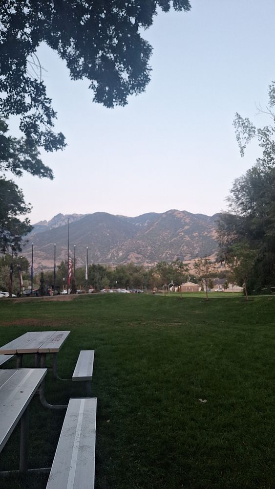A serene park scene featuring mountains in the background and picnic tables in the foreground.