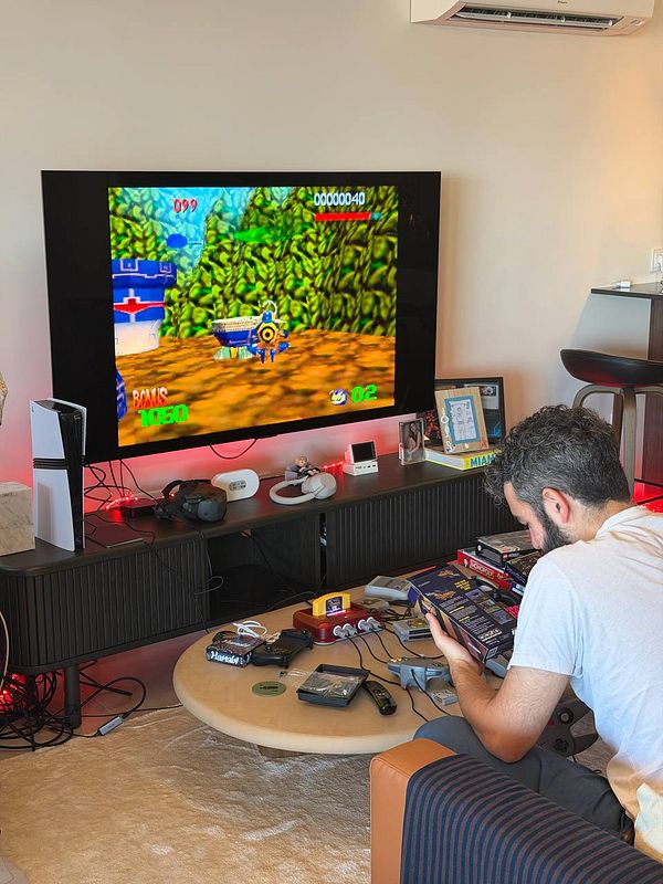 A man engages with retro gaming equipment in a living room featuring a video game displayed on a mounted television.