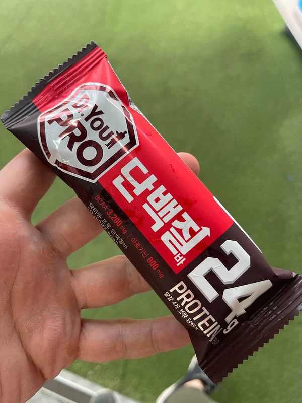A hand holding a protein bar with a red and black wrapper.