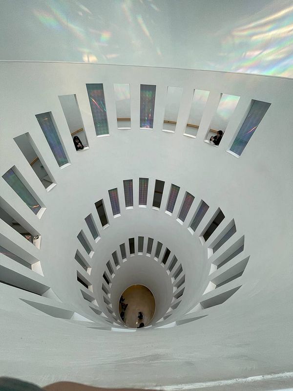 A spiral staircase with a modern design, featuring large cut-out windows and reflections of light.