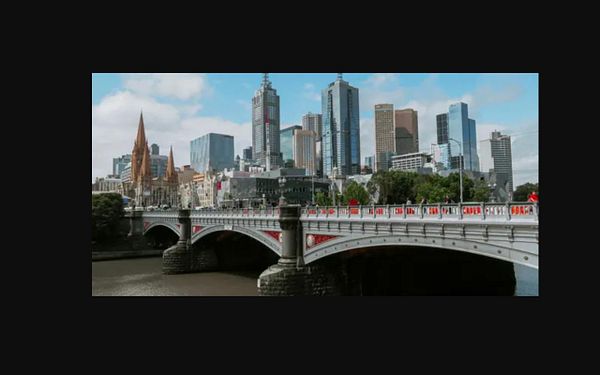 A nighttime cityscape with illuminated buildings and streetlights, displayed in a landscape orientation and exhibiting low resolution with pixelation.