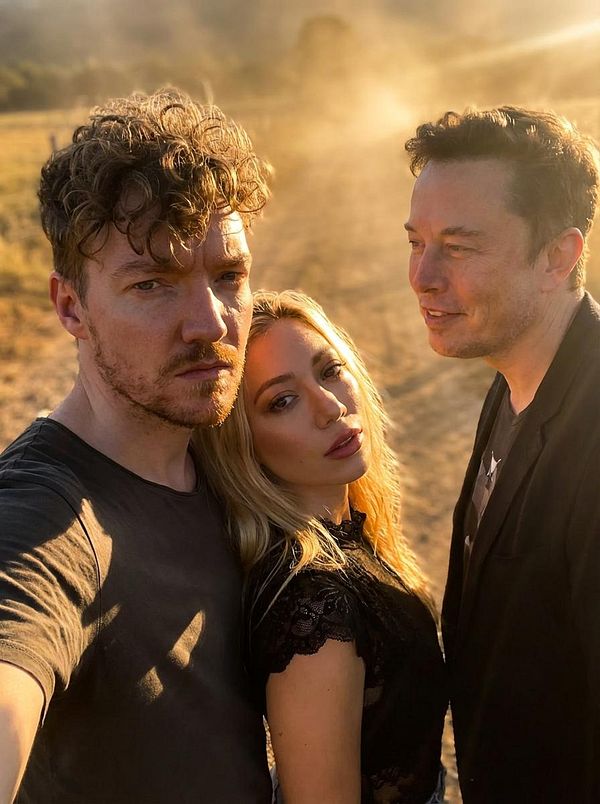 A selfie featuring three individuals in a sunlit outdoor setting with a dusty background.