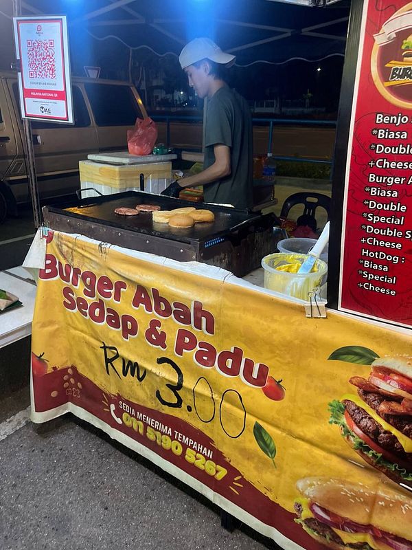 A large burger with multiple layers including lettuce, tomato, bacon, cheese, and a beef patty on a sesame seed bun.