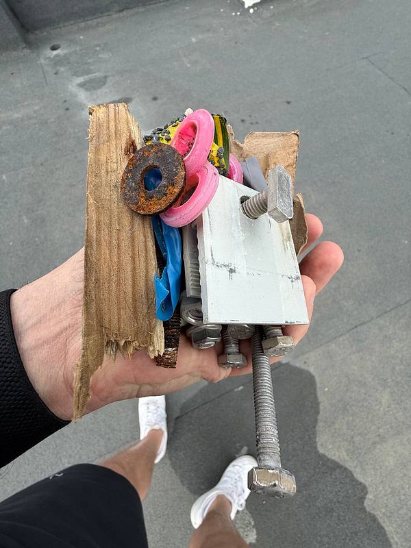 A hand holds a collection of assorted hardware and debris found on a roof.