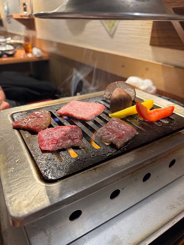 Grilled wagyu beef and vegetables on a tabletop grill in a restaurant setting.