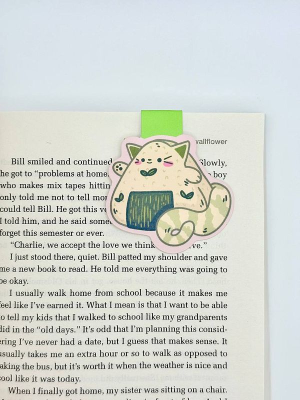 A cute magnetic bookmark featuring a cartoon cat is placed on an open book page.