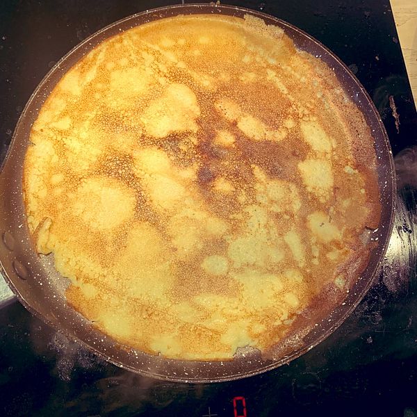 A golden-brown crepe is cooking in a frying pan on a stovetop.